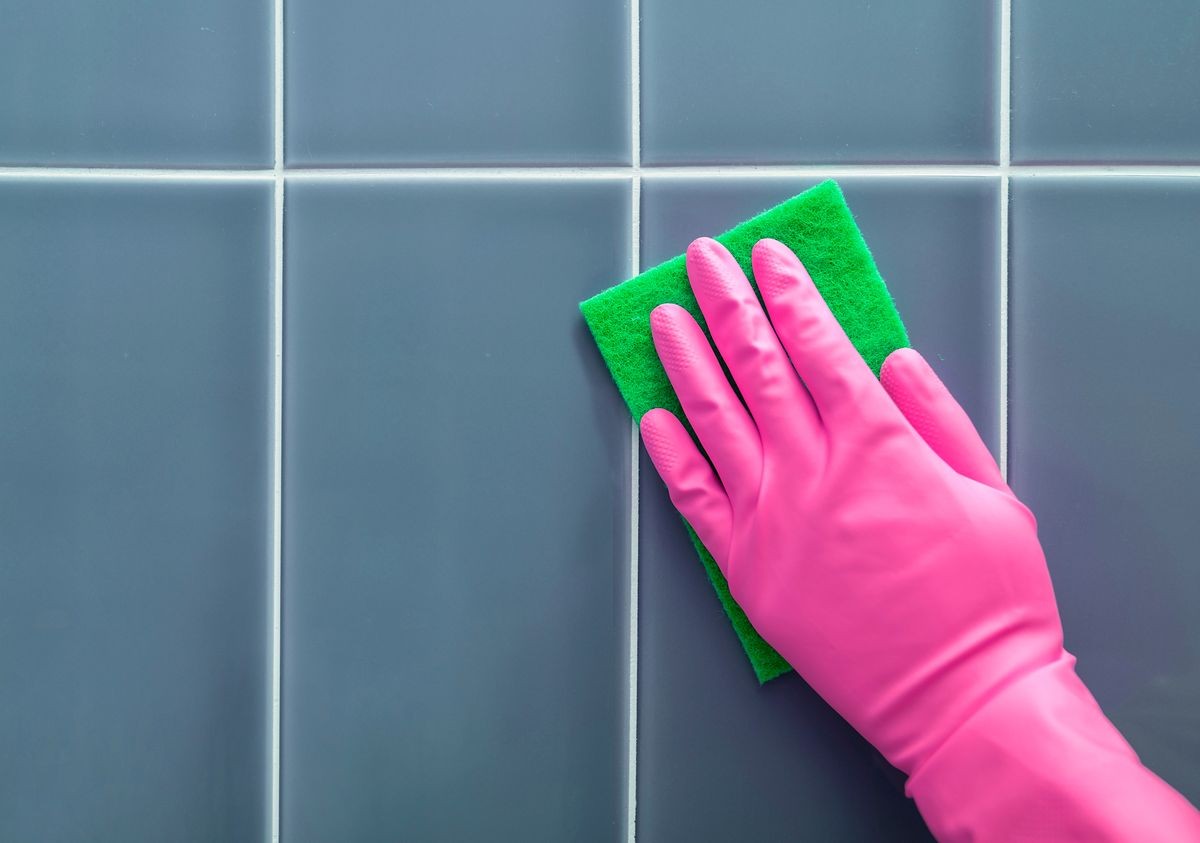 Hand in rubber gloves washes a tile.